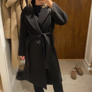 Svart kappa med knytband - Snygg svart kappa med knytband i midjan. Perfekt för kyligare dagar med sin långa design och klassiska look. Ett måste i garderoben för en stilren outfit.