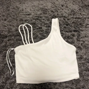 Vit oneshoulder topp från Bershka - Snygg vit oneshoulder topp från Bershka med ribbad textur. Perfekt för en trendig look med sina unika axelband. Tillverkad i Marocko.