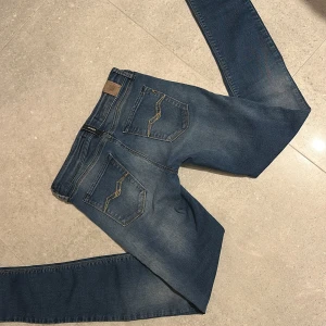Blå jeans från Replay - Snygga blå jeans från Replay med klassisk femficksdesign och knappgylf. Perfekta för en avslappnad stil med en touch av elegans. Märkesdetaljer på fickorna och bältesslingorna ger en extra stilpoäng. Kan förhandla om pris 