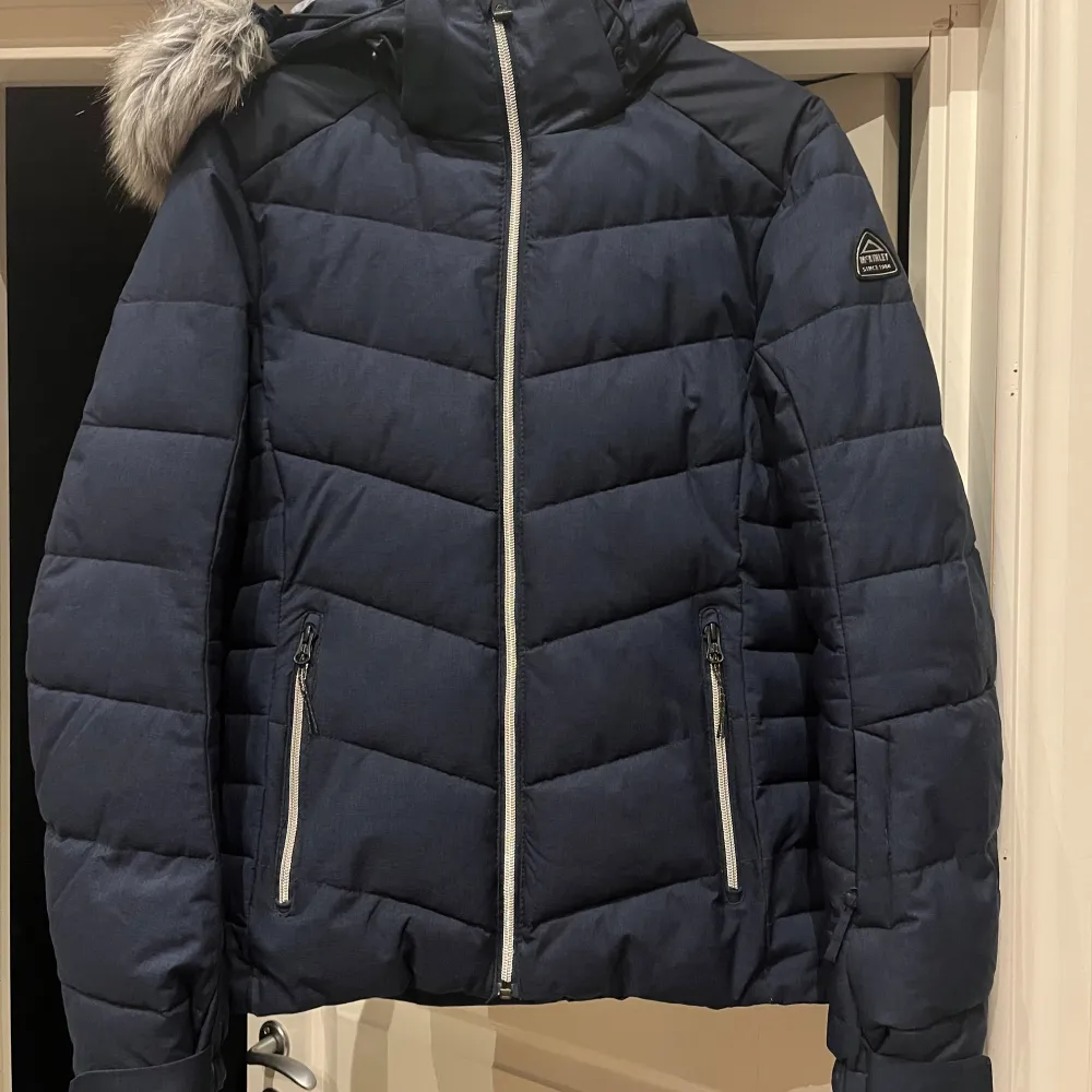 Snygg blå dunjacka från McKinley med avtagbar huva och fuskpälsdetalj. Jackan har dragkedja framtill och två praktiska fickor med dragkedjor. Perfekt för kyliga dagar.. Takit.