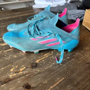 Adidas x speedflow elite blåa, Storlek 39 1/3 - Snygga fotbollsskor från Adidas i en fräsch blå färg med rosa detaljer. Skorna har snörning och en lättviktig design för optimal prestation på planen. Perfekta för dig som vill sticka ut med stil. 7/10 betyg. Jag köpte skorna för 2500 kr och använda i ungefär 3 månader. 