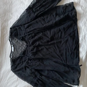 Svart blus från Vila - Snygg svart blus från Vila med prickigt mönster och transparenta detaljer. Blusen har trekvartsärmar och en luftig passform, perfekt för en stilren look.