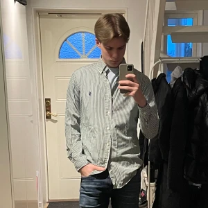 Randig skjorta från Ralph Lauren - Snygg och stilren randig skjorta från Ralph Lauren i grönt och vitt. Skjortan har långa ärmar och knappar framtill. Perfekt för en klassisk look. Nästan aldrig använd!