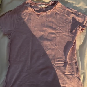 Lila t-shirt från Zara - Säljer en lila t-shirt från Zara i mjukt material. T-shirten har korta ärmar och en enkel design med rund halsringning. Perfekt för en avslappnad stil och är perfekt att träna i.