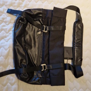 Svart axelväska från Don Donna - Snygg svart axelväska från Don Donna med justerbar axelrem och praktiska spännen. Väskan har en dragkedja framtill och är tillverkad i syntetmaterial. Perfekt för en stilren look.