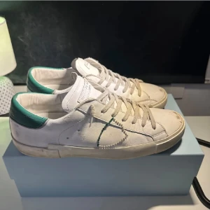 Vita sneakers med gröna detaljer - Säljer ett par riktigt snygga phillipe model väldigt bra skick. Skon är vit med snygga gröna detaljer enligt mig.     Stl 42