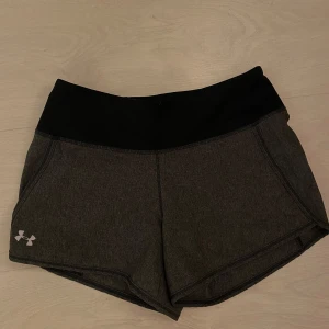Grå träningsshorts från Under Armour - Säljer ett par grå träningsshorts från Under Armour. De är tillverkade i polyester och har en bekväm passform med elastisk midja. Perfekta för träning och andra aktiviteter.