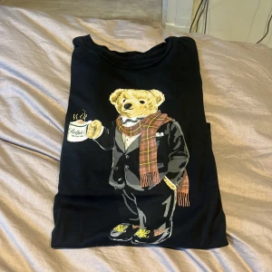 Ralph lauren  -  En svart tröja med en av Ralph lauren björnarna som håller i en kaffekopp  jag är ca 158 cm lång  Och  den passar perfekt 🤩 ! 