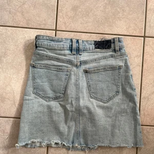 Jeanskjol i ljus denim - Säljer en snygg lågmidjad jeanskjol i ljus denim. Den har en rå kant nertill för en cool och avslappnad look. Kjolen har klassiska fem fickor och en knapp med dragkedja framtill. Perfekt för sommardagar eller en avslappnad utekväll. Passar bra med en t-shirt eller en stickad tröja! skriv vid frågor💗
