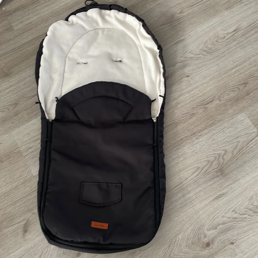 Säljer en mysig svart åkpåse från Sensillo, perfekt för barnvagnen. Den är fodrad med ull för extra värme och komfort. Åkpåsen har en praktisk dragkedja och en ficka framtill. Måtten är 95x40 cm.. Muu.