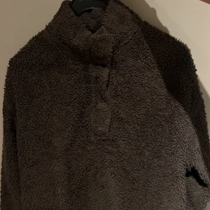 Brun fleece tröja - Mysig brun fleece tröja med hög krage. Perfekt för kyliga dagar med sin mjuka och varma textur. Tröjan har en enkel design utan mönster och långa ärmar.