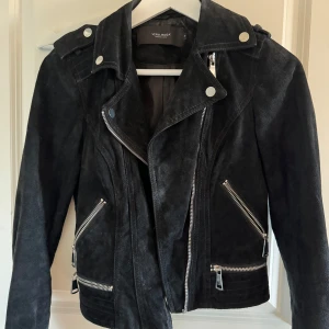 Svart mockajacka från Vero Moda - Snygg svart mockajacka från Vero Moda med dragkedjor och knappar. Jackan har en cool bikerstil med flera fickor och detaljer. Perfekt för att ge din outfit en edgy touch.