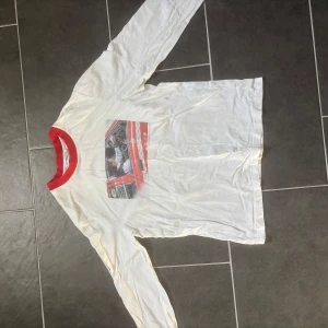 Vit långärmad t-shirt från Axel Arigato - Cool vit långärmad t-shirt från Axel Arigato med röd krage och tryck av en bil med texten 'Somewhere in Tokyo'. Ärmen har ett stilrent arigatotryck i rött.