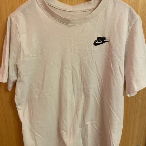 Vit t-shirt från Nike - Säljer en klassisk vit t-shirt från Nike med deras ikoniska logga broderad på bröstet. Perfekt för en avslappnad stil. T-shirten är kortärmad och gjord i mjuk bomull för extra komfort.