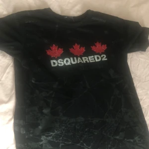 Svart t-shirt från Dsquared2 - Snygg svart t-shirt från Dsquared2 med glittrande logotyp och röda lönnlöv på bröstet. Perfekt för en stilren look med en touch av bling. Kortärmad och bekväm passform.