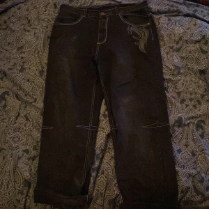 Svarta jeans med broderade detaljer - Unika svarta jeans med coola broderade vingar och bokstaven 'H' på baksidan. Jeansen har en loose passform och är dekorerade med kontrastsömmar. Perfekta för dig som vill sticka ut med en edgy stil.