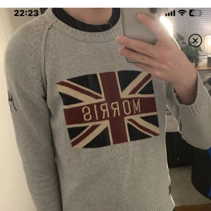 Grå tröja från Morris med Union Jack-motiv - Snygg grå tröja från Morris med ett stort Union Jack-motiv och texten 'Morris' på bröstet. Tröjan har långa ärmar och en broderad detalj med 'MG 1968' på ärmen. Perfekt för en stilren look. Använt tröjan ett par fåtal gånger men mycket bra skick    Nypris runt 1800kr!  Mitt pris 400!   Hör av er vid funderingar 