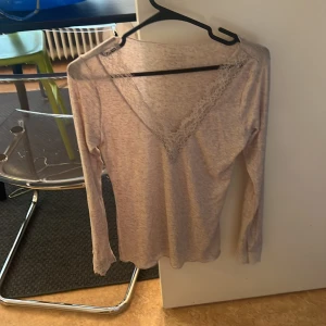Beige långärmad topp från Intimissimi - Säljer en elegant beige långärmad topp från Intimissimi i mjukt material med kashmir. Toppen har en v-ringad design med spetsdetaljer vid halsen och ärmsluten. Perfekt för en stilren look.
