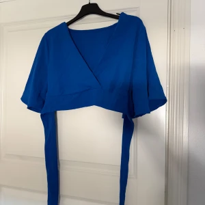 Blå omlottopp - Snygg blå omlottopp med korta ärmar och knytband i midjan. Toppen har en v-ringad design och är croppad.