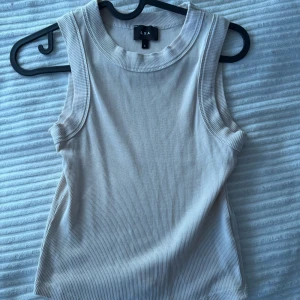 Beige ribbad linnetopp från Lxa - Säljer en stilren beige ribbad linnetopp från Lxa. Toppen är ärmlös och har en rund halsringning, perfekt för varma dagar eller som lager under en jacka.
