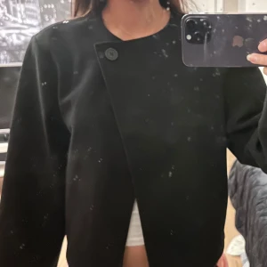 Svart kavaj med knapp - Snygg svart kavaj med en unik asymmetrisk knäppning framtill. 