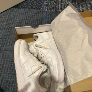 Vita Nike Air Force  - Säljer ett par klassiska vita Nike Air Force sneakers. Skorna har en stilren design med snörning och den ikoniska Nike-loggan på sidan. Perfekta för en casual look.