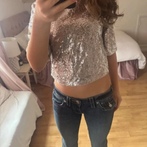 Glittrig topp - Säljer en glittrig topp i silver med paljetter. Toppen har korta ärmar och en rund halsringning. Perfekt fest topp. Kommit till användning vid ett tillfälle 