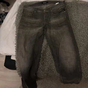 Grå jeans från Replay - Snygga grå jeans från Replay med klassisk femficksdesign. De har en knappgylf och är perfekta för en avslappnad stil. Jeansen har en diskret tvättad look som ger dem en cool touch.