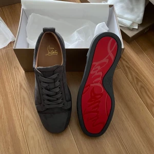 Grå sneakers från Christian Louboutin - Snygga grå sneakers i mocka från Christian Louboutin med den ikoniska röda sulan. Skorna har snörning och en stilren design som passar perfekt för en trendig look .Priset kan diskuteras.