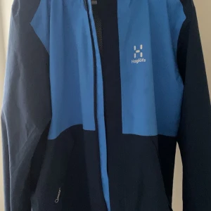 Haglöfs jacka, storlek M - Haglöfs jacka i blått och svart. Riktigt bra och enkel jacka. Jackan har en huva och en dragkedja framtill. Den är i fint skick. Nypris 1499kr passa på. Perfekt för utomhusaktiviteter med sin funktionella design och stilrena look.