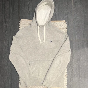 Polo Ralph Lauren Hoodie Grå - Riktigt snygg Hoodie från Ralph Lauren || Storlek: M || Mycket fint skick (förutom ett reva på ryggen som dock ej syns under användning då luvan är för) 
