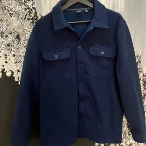 Mörkblå overshirt med knappar - Snygg mörkblå overshirt med knappar framtill och två bröstfickor med lock. Perfekt för lager-på-lager-stil. Klassisk krage och långärmad design.