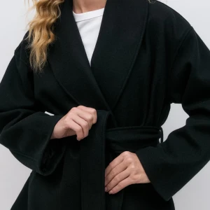 Svart kappa med knytband - Elegant svart kappa med knytband i midjan och bred krage. Perfekt för en stilren look under kyligare dagar. Den har långa ärmar och en klassisk design som passar till många tillfällen.