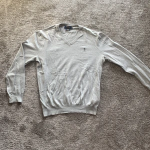 Grå tröja från Polo Ralph Lauren - Säljer en stilren grå tröja från Polo Ralph Lauren i slim fit. Tröjan är tillverkad av mjuk Pima bomull och har en soft v-ringad krage. Den är i väldigt gott skick. 