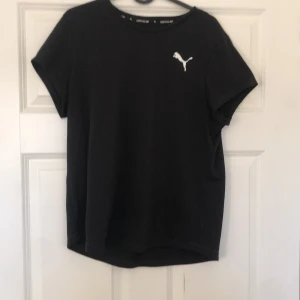 Svart träningströja från Puma - Säljer en svart tränings-t-shirt från Puma med deras ikoniska logga i vitt på bröstet. T-shirten har en klassisk rund hals och korta ärmar, perfekt för en sportig look. Tillverkad i ett mjukt och bekvämt material. Storlek är XL men sitter bra på mig som är M-L och passar även xs-s om man vill ha en lagom t-shirt🥰🥰
