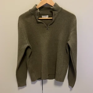 Olivgrön stickad tröja från These Glory Days - Säljer en olivgrön stickad tröja från These Glory Days. Tröjan har en dragkedja vid halsen och långa ärmar. Perfekt för kyligare dagar med sin mysiga och stilrena design.