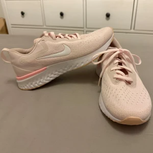 Nike sneakers i ljusrosa - Snygga ljusrosa Nike sneakers med vit sula och diskreta detaljer. Perfekta för en sportig look med bekväm passform och snörning. Sulan har ett mönster i vitt och rosa för extra grepp.