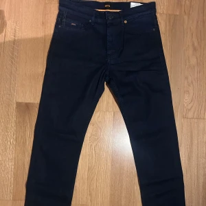 Mörkblåa Jeans från Boss - Snygga mörkblå jeans från Boss i slim fit. Klassisk design med fem fickor. Perfekta för en stilren look. HELT NYA.  Modellen 'DELAWARE'. Storlek W30 L32. NYPRIS 1099
