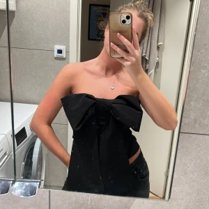 Topp NAKD - En svart topp i storlek S med en stor rosett i fronten. Är gummi på överdelen så den inte faller ner. Använd 1 gång, köpt denna vinter.