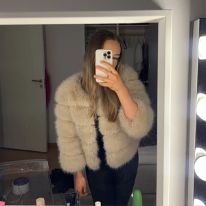 Beige pälsjacka - Säljer en fluffig beige pälsjacka med hakknäppning. Jackan har en elegant och lyxig look, perfekt för att hålla sig varm och stilren under kyliga dagar. Använd endast en gång, ny pris 1300kr
