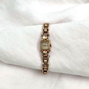 Elinor - Elegant guldfärgad klocka - Klockan Elinor från märket Eko är en mekanisk klocka. En smakfull guldfärgad klocka med fyrkantig urtavla och länkarmband. Strålande accessoar för att lyfta din stil.

 Omkrets 18 eller 17cm Urets bredd 1,5cm Längd 19,5 cm