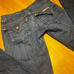 Hudson jeans  - Snygga mörkblå jeans från Hudson med dubbla knappar och dragkedja. De har en fin bootcut. Knappen på ena bakfickan har lossnat därmed sänkt pris (går att laga) Innerbenlängd: 79 cm och midja: 38 cm (notera att materialet är hyfsat stretchig så skulle passa midjor från 35-40) 🫶