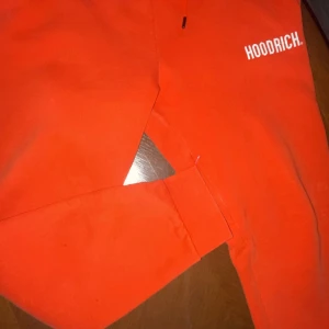 Orange mjukisbyxor från Hoodrich - Snygga orange mjukisbyxor från Hoodrich med justerbar snörning i midjan. Perfekta för en avslappnad stil med en cool logga på benet. Passar utmärkt för chill dagar.