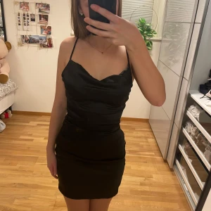 Svart satin klänning - Säljer denna jättefina svarta satin klänning med smala axelband och en figursydd passform. Den har en kortare längd och den har en diskret dragkedja på sidan. Säljer denna då den endast användes vid ett tillfälle. Klänningen är köpt från en butik i Kungsbacka som jag inte minns namnet på, där de hade olika fina klänningar. Men i klänningen så står ett märke, ”JJXX”.