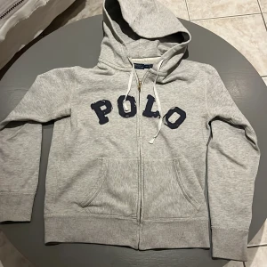 Fet ralph lauren zip hoodie - Säljer min grå hoodie från Ralph Lauren med zip, denna hoodie är extremt unik och eftertraktad. Har fått många som frågat var ja köpte den. Hoodie är i storlek S och har passat mig fram tills nu då jag tyvärr växt ur den. Den e perfekt för dig som vill hänga på trenden med nya unika raffe hoodies! Designen på hoodien ska vara så lite distressed, inget som jag gjort på bokstäverna, kom pm för fler bilder på det!