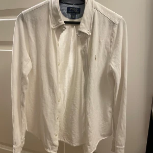Skjorta Ralph Lauren  - Snygg vit skjorta från Polo Ralph Lauren med klassisk krage och broderad logotyp på bröstet. Skjortan har långa ärmar och knappar framtill. XL i junior motsvarar S/Xs