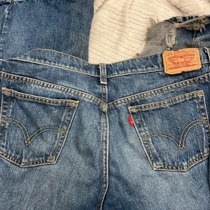 Blå Levis jeans - Klassiska blå Levis jeans med slitna detaljer och ikonisk läderpatch på baksidan. Perfekta för en avslappnad stil.