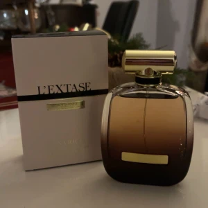 L'Extase parfym från Nina Ricci - Elegant parfymflaska med en lyxig design i guld och mörkbrunt glas. L'Extase från Nina Ricci är en sensuell doft som kommer i en stilren förpackning. 