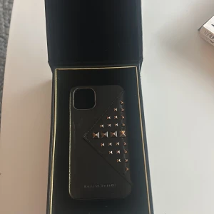 Svart mobilskal från iDeal of Sweden - Snyggt svart mobilskal från iDeal of Sweden med stilrena nitar i guld. Skalet har en elegant design och kommer i en lyxig förpackning. Perfekt för att ge din telefon ett trendigt utseende.