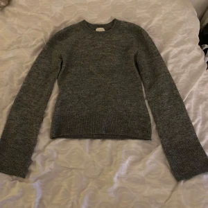 Grå stickad tröja - Säljer en mysig grå stickad tröja med rund hals och långa ärmar. Perfekt för kyliga dagar och enkel att matcha med olika outfits. Tröjan har ribbstickade muddar vid ärmslut och nederkant.